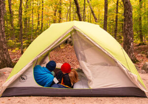 a couple sitting inside a tent, which is pitched on a durable surface in a campground