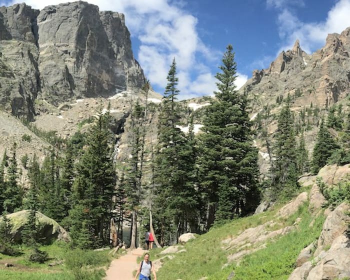 Person hiking in a park with high cliffs and tall pines