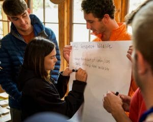 A woman writes on a piece of paper held by a man during a group discussion.