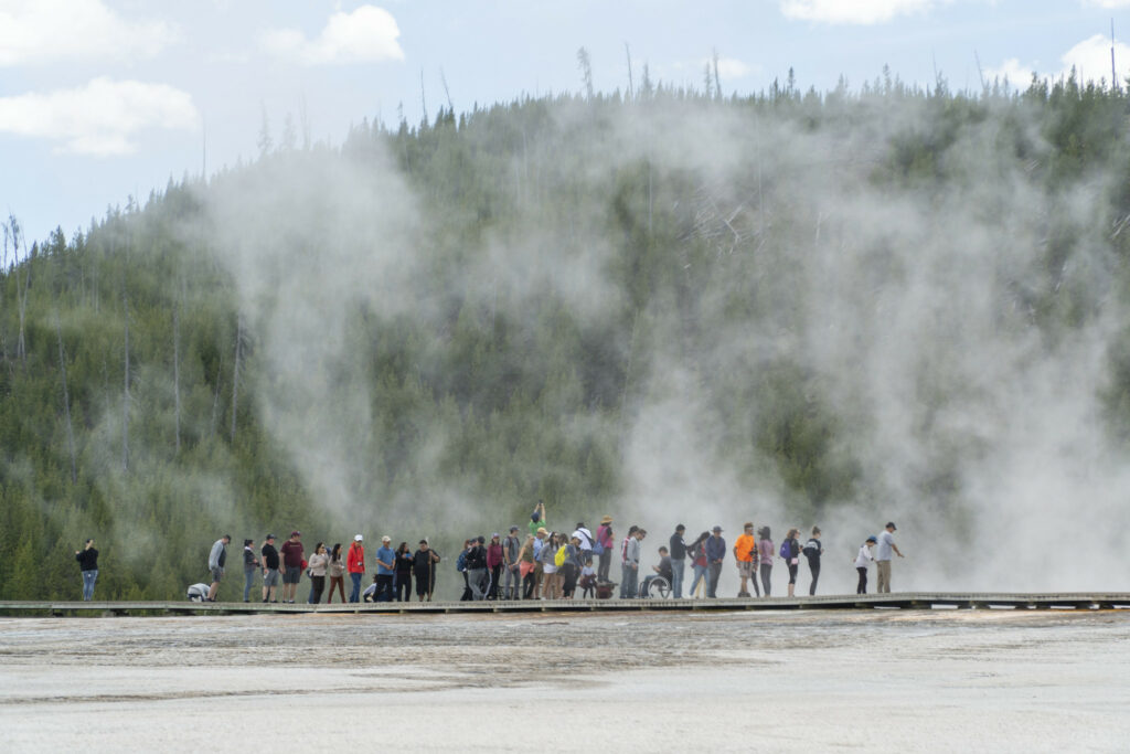 a group of people hiking next to thermal pools with steam rising
