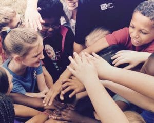 A bunch of kids putting their hands on top of each others hands in the middle of a circle during an activity.